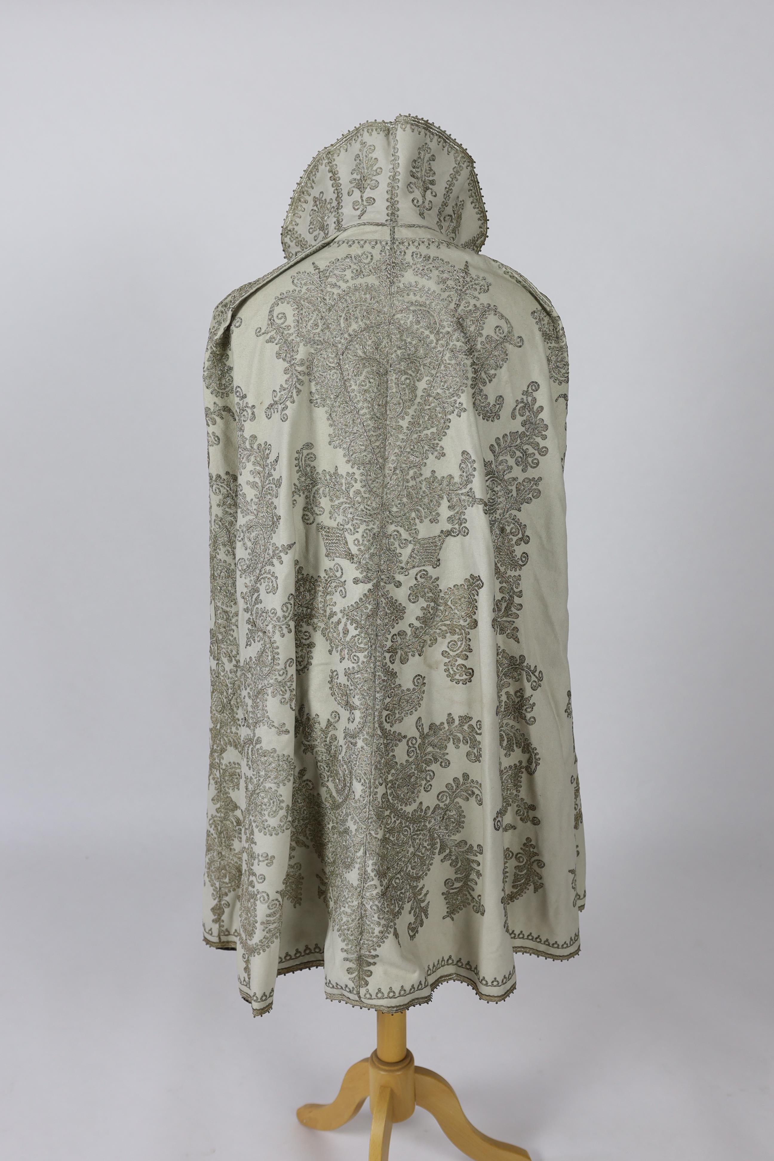 A 19th century Indian fine cream wool embroidered cape, probably made for the European market, embroidered in panels of silver metallic thread in an ornate vertical design with turquoise embellishments and lined in black